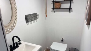 Un baño pequeño con un lavamanos blanco, un inodoro, un espejo y una repisa con una cesta.