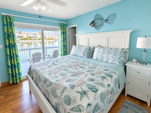 A bedroom with a bed, a nightstand, a lamp, a ceiling fan, and a view of a pool and buildings. - 3- Min Walk to Private Beach •Lakefront •Major Snowbird Discounts—Message Us! (Destin)