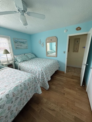 A bedroom with two beds, a ceiling fan, a window with blinds, a bedside table, a wall clock, and a door leading to another room. - NEW! • Lakefront • Short Walk to Private Beach • Monthly Snowbird Discounts (Destin)