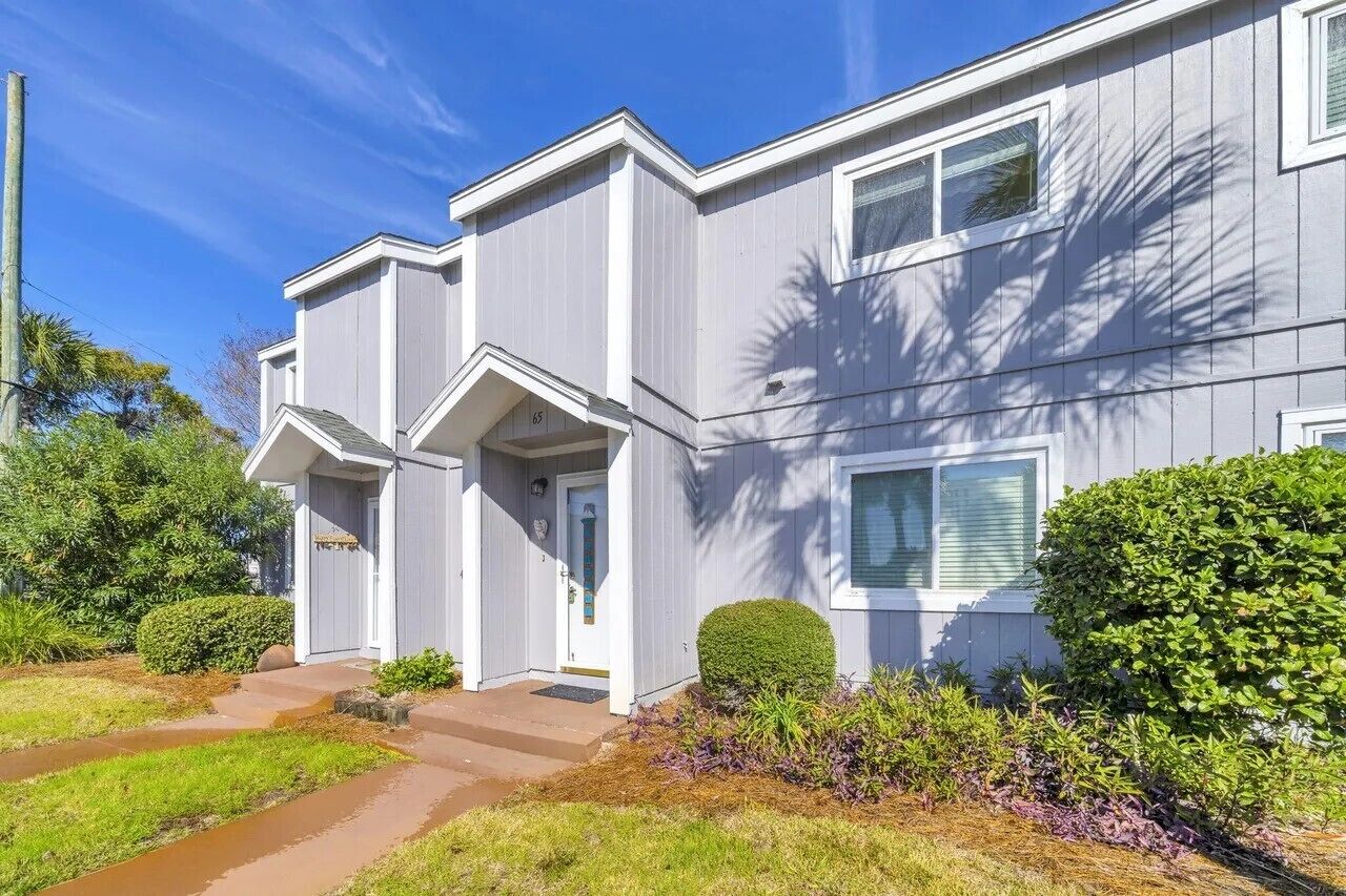 A two-story residential building with a front porch, a garage, and a well-maintained lawn.