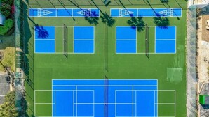 An aerial view of a tennis court complex with multiple courts, surrounded by greenery and a fence. - Lakefront Townhome.  Steps to Private Beach. Large Decks (Destin)
