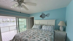 A bedroom with a bed, a nightstand, a lamp, a ceiling fan, and a view of a water body through a sliding door. - Lakefront Townhome.  Steps to Private Beach. Large Decks (Destin)