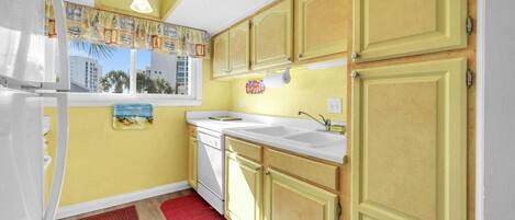 A compact kitchen with a refrigerator, sink, and wooden cabinets.