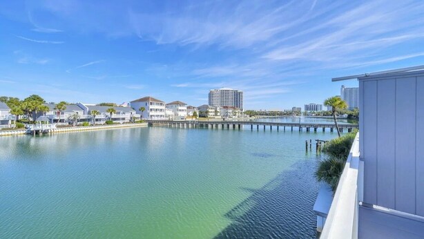 A waterfront property with a dock, a clear blue sky, and buildings in the background. - Lakefront Townhome.  Steps to Private Beach. Large Decks (Destin)