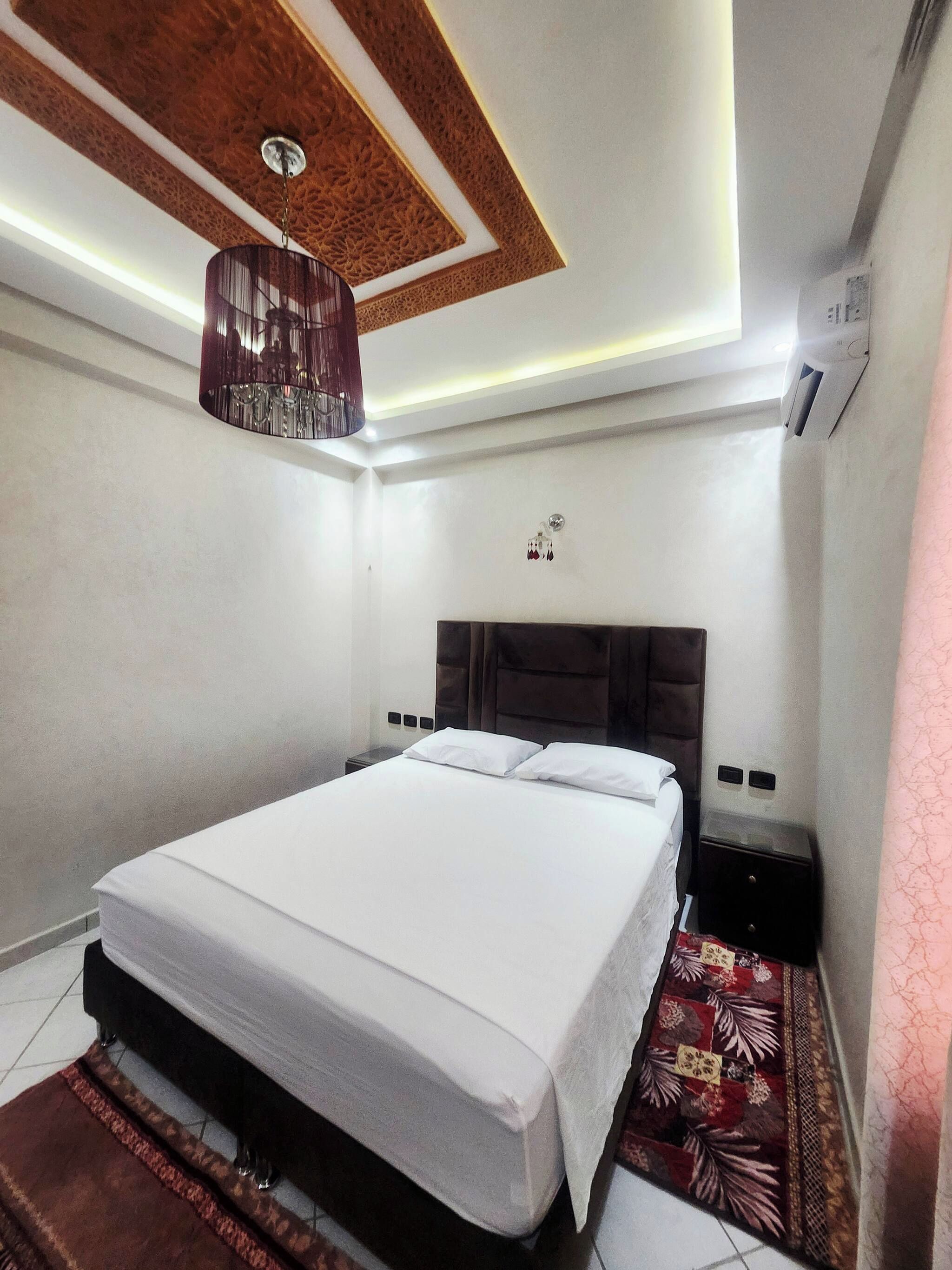 Habitación de hotel con cama, lámpara colgante, aire acondicionado de pared y alfombra estampada.