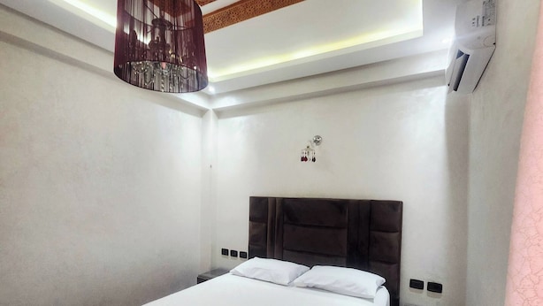 A hotel room with a bed, a hanging light fixture, a wall-mounted air conditioning unit, and a patterned rug. - Modern & Spacious Apartment in Guéliz - Parking (Marrakech)
