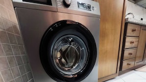 A front-loading washing machine in a kitchen with tiled flooring and wooden cabinets. - Modern & Spacious Apartment in Guéliz - Parking (Marrakech)