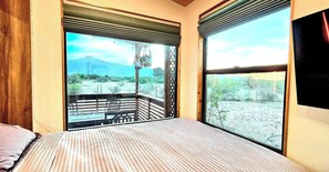 Una stanza con un letto, una finestra vista su un paesaggio desertico e un balcone con ringhiera.