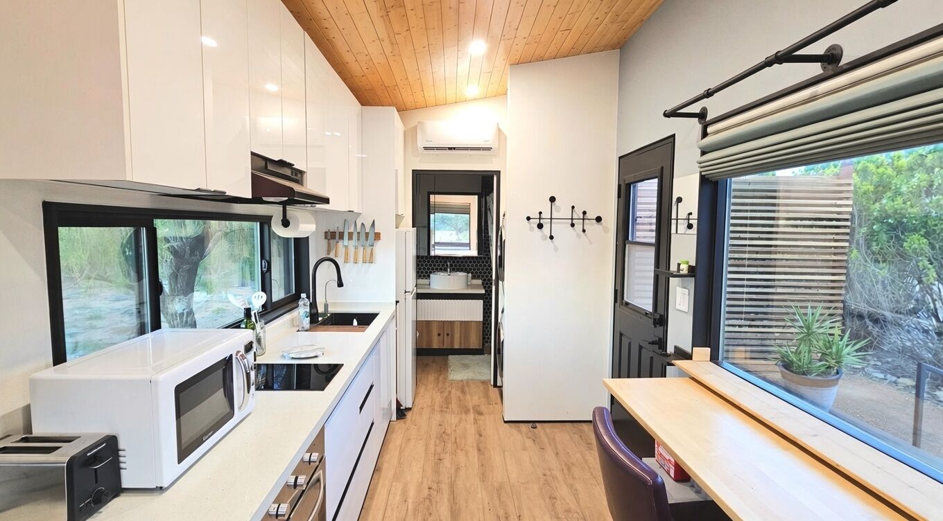 Eine moderne Küche mit Mikrowelle, Toaster und Spüle. Es gibt eine Holzbalkendecke und ein Fenster mit Jalousien.