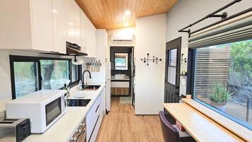 Eine moderne Küche mit Mikrowelle, Toaster und Spüle. Es gibt eine Holzbalkendecke und ein Fenster mit Jalousien.