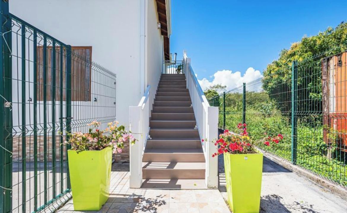 A staircase leading to a building with a white exterior, surrounded by a green fence and potted plants.