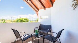 Ein Balkon mit Tisch und Stühlen, einem Blumentopf und Blick auf Grünflächen und Gebäude.