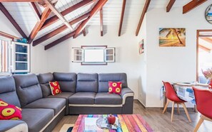 Ein Wohnzimmer mit einer Eckcouch, einem Esstisch mit Stühlen, einem farbenfrohen Teppich und einer Holzbalkendecke.