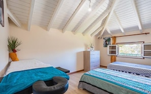 Ein Schlafzimmer mit zwei Betten, einem Schminktisch, einem Fenster mit Vorhängen und einer Decke mit sichtbaren Balken.