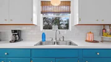 Una cucina con mobili bianchi, un piano di lavoro blu, una finestra con persiane, una macchina da caffè e un lavello.