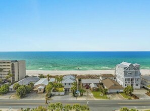 Una zona residencial costera con propiedades frente a la playa, una carretera y una vista despejada del océano.