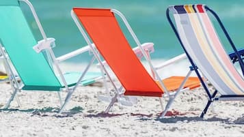Tre sedie da spiaggia con struttura in metallo e sedili in tessuto, disposte su una spiaggia sabbiosa con vista sull'oceano.