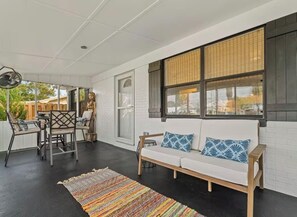 A covered outdoor seating area with a sofa, chairs, and a dining table.