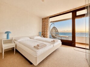 Ein Schlafzimmer mit einem Bett, einem Nachttisch, einem Hängekorbstuhl und Meerblick.