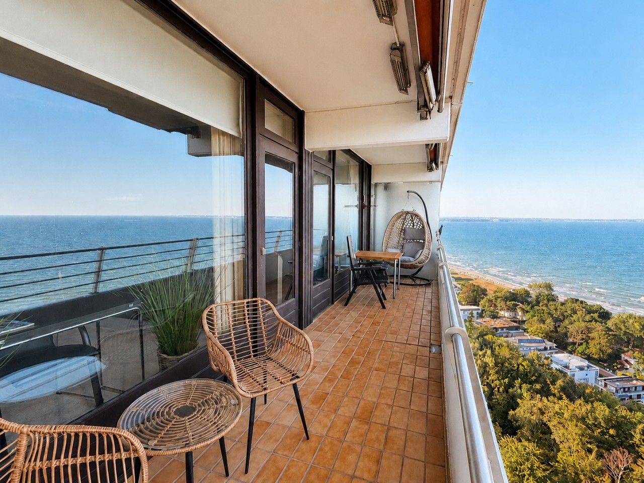 Un balcón con sillas de mimbre, una mesa y vistas al mar y edificios.