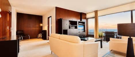 Una sala de estar moderna con un sofá, una mesa de centro y un televisor. Hay un ventanal con vista al océano.