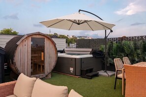 Ein Whirlpool mit Baldachin, eine hölzerne Fasskonstruktion und eine Terrasse mit Stühlen und Tisch.