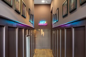 Un couloir aux murs ornés de tableaux encadrés, une enseigne au néon indiquant « Hype Country », et une porte au fond.