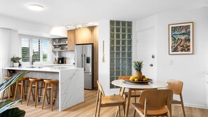 Een moderne keuken met een centraal eiland, houten barkrukken en een eethoek met een ronde tafel en stoelen.