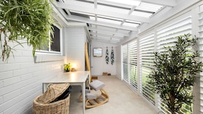 Ein sonnendurchflutetes Zimmer mit einer weißen Backsteinwand, einer hölzernen Bank, einem kleinen Tisch mit einer Pflanze und einem Blumentopf mit Baum.