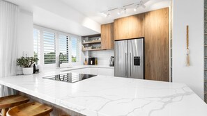 A modern kitchen with a large island, stainless steel appliances, and wooden cabinetry. - Ocean Shores 10 Peregian Beach (Peregian Beach)