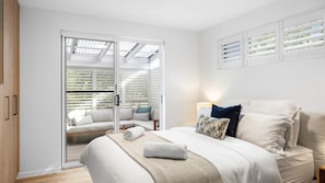 Een slaapkamer met een bed, nachtkastje, lamp en uitzicht door een schuifdeur op een balkon met een bank.