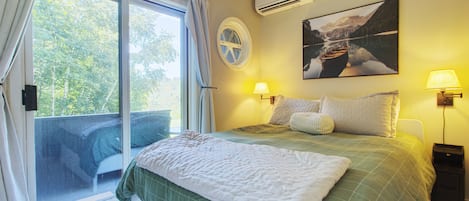 Un dormitorio con cama, dos lámparas de noche, una ventana con cortinas, aire acondicionado de pared y un cuadro de un barco en el agua.