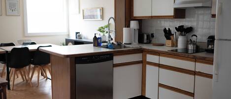 A modern kitchen with wooden cabinets, a dishwasher, and a dining area with chairs.