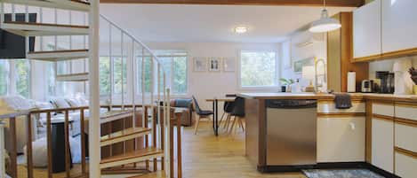 A modern kitchen with a dishwasher, a dining area with a table and chairs, and a staircase with wooden railings.