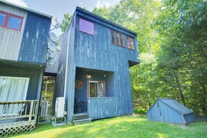 A two-story wooden cabin with a deck, satellite dishes, and a small shed. - Enjoy this sunlit condo in Waterville Estates with amazing mountain views! (Campton)