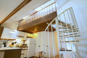 A kitchen with wooden beams, a white staircase, and a view of the upper floor. - Enjoy this sunlit condo in Waterville Estates with amazing mountain views! (Campton)