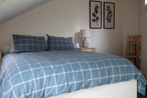 Ein Schlafzimmer mit einem Bett, Kissen, einem Nachttisch, einer Lampe und zwei gerahmten Wandbildern.