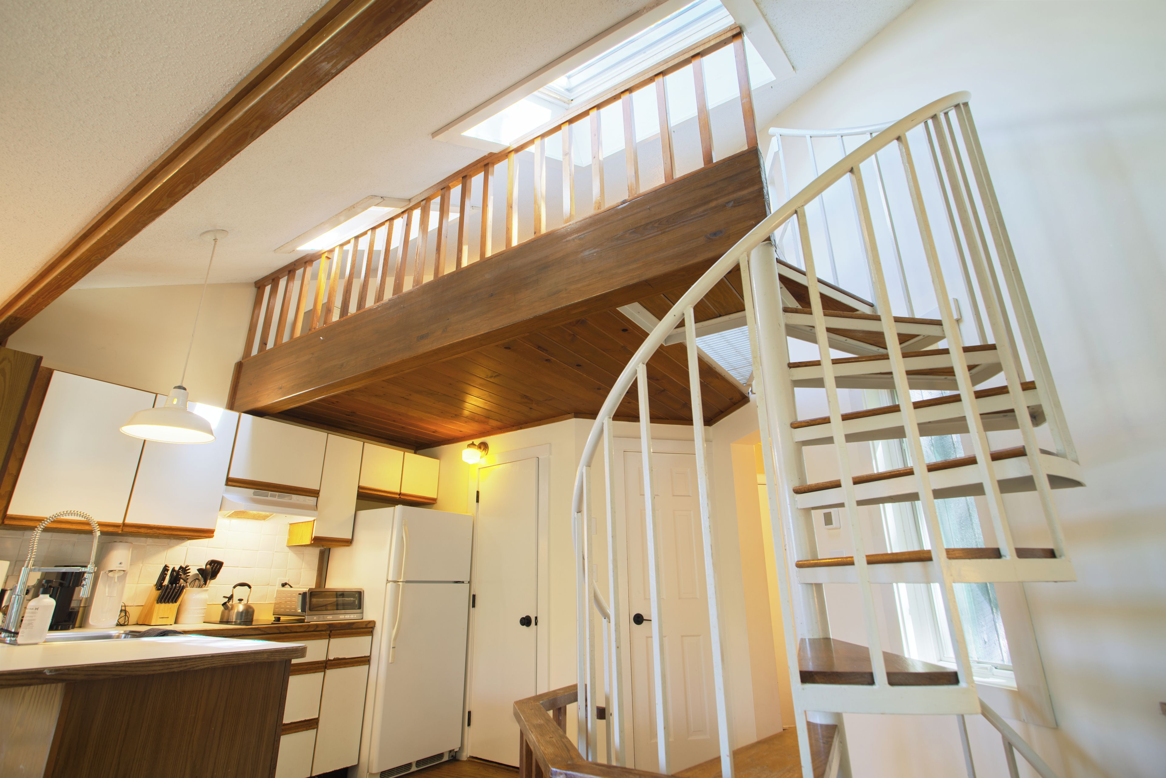 Une cuisine avec des poutres en bois, un escalier blanc et une vue sur l’étage supérieur.
