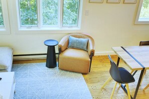 Ein Zimmer mit Ledersessel, kleinem runden Tisch, Esstisch mit Stühlen und einem gemusterten Teppich.