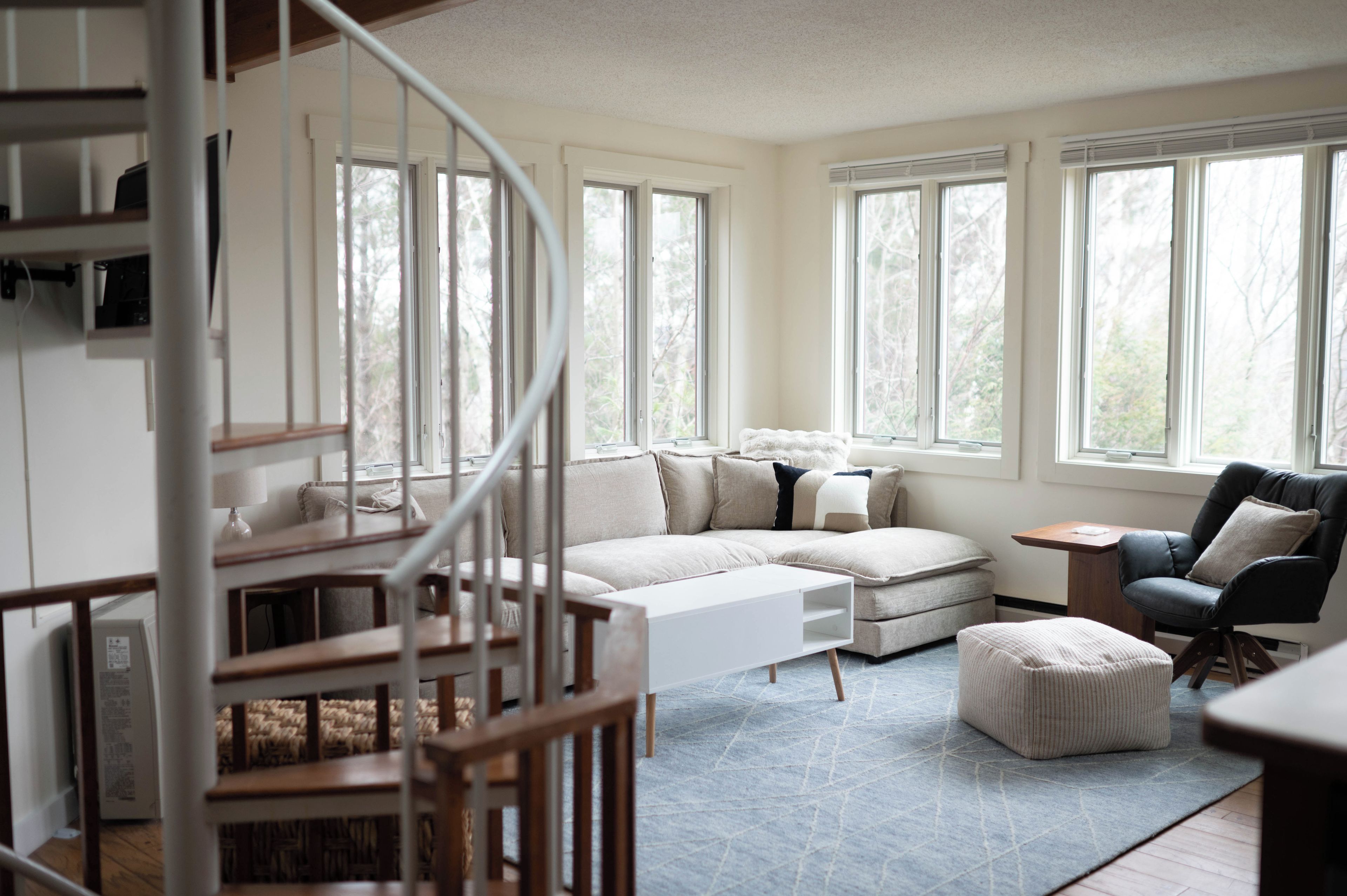 A spacious living room with a large sectional sofa, a small table, a chair, and a staircase leading to an upper level.