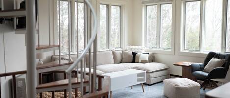 A spacious living room with a large sectional sofa, a small table, a chair, and a staircase leading to an upper level.
