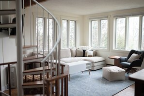 Ein geräumiges Wohnzimmer mit einer großen Eckcouch, einem kleinen Tisch, einem Sessel und einer Treppe, die in ein Obergeschoss führt.