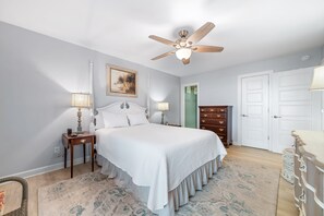 A bedroom with a bed, two bedside tables, a ceiling fan, a painting, a dresser, and a door. - Gulf Front | Huge Balcony | Direct Beach Access | BEACHBALL PROPERTIES (Orange Beach)