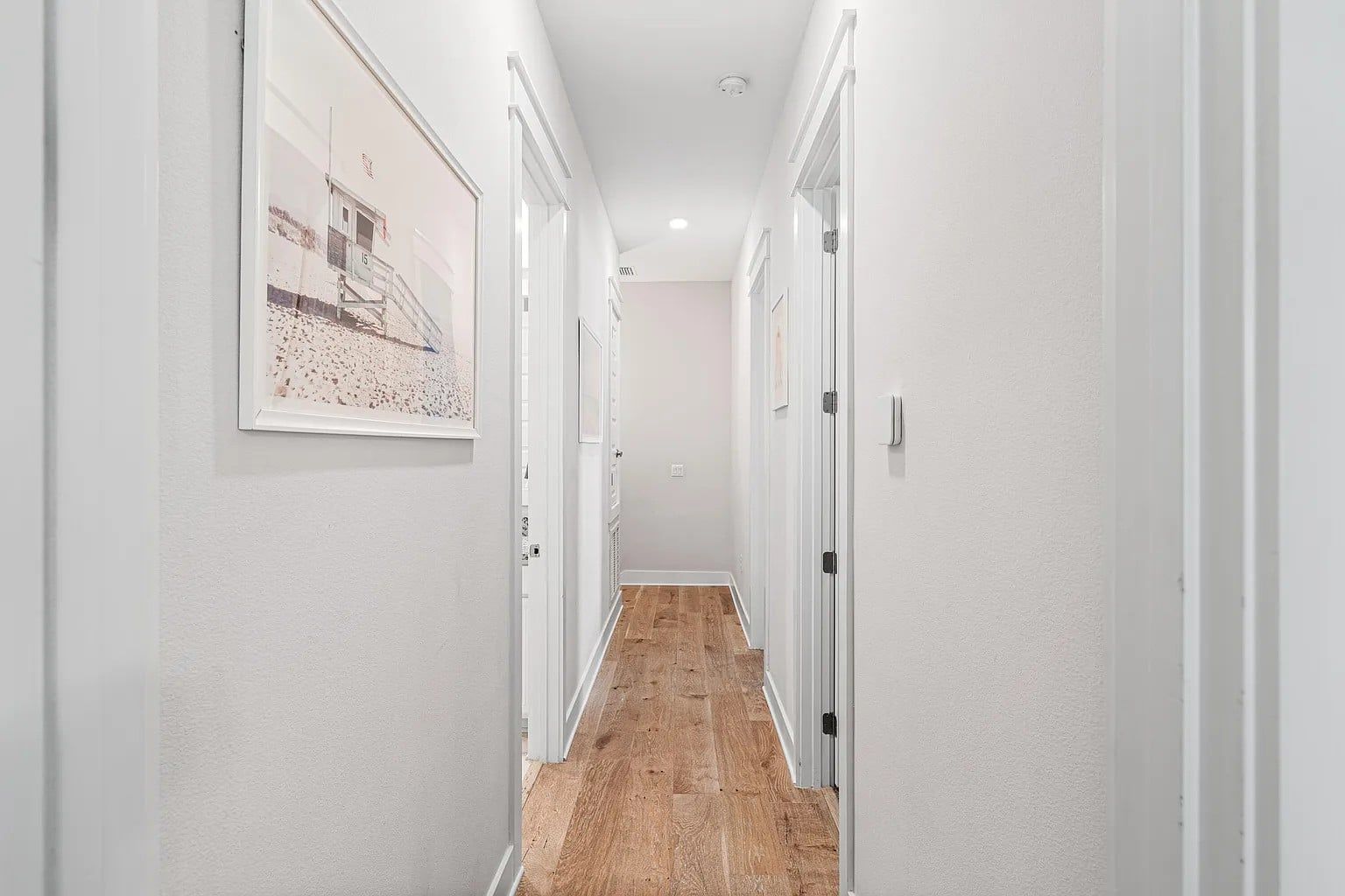 Un couloir aux murs blancs, doté d’un plancher en bois et de portes donnant accès aux différentes pièces.