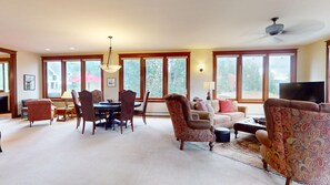 A spacious living room with a dining area, large windows, and a ceiling fan. - Butte View Chalet - Sleeps 10 (Crested Butte)