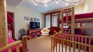Una habitación con literas, televisor, una silla y una mesita.