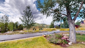 A road with a tree-lined path, a grassy area, and a hilly landscape in the background. - Butte View Chalet - Sleeps 10 (Crested Butte)
