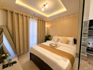 Una camera d'albergo con un letto, un comodino con un vaso di fiori, uno specchio e una finestra con tende.