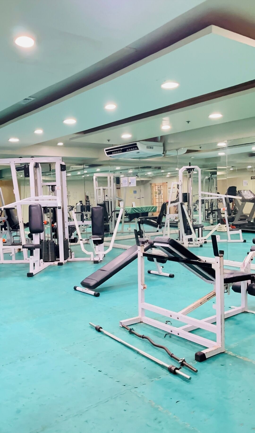 Ein Fitnessstudio mit unterschiedlichen Trainingsgeräten, einer Spiegelwand und einer Decke mit eingelassener Beleuchtung.