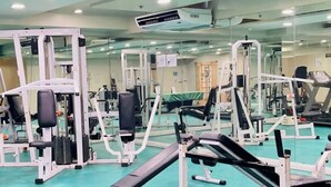 Ein Fitnessstudio mit unterschiedlichen Trainingsgeräten, einer Spiegelwand und einer Decke mit eingelassener Beleuchtung.